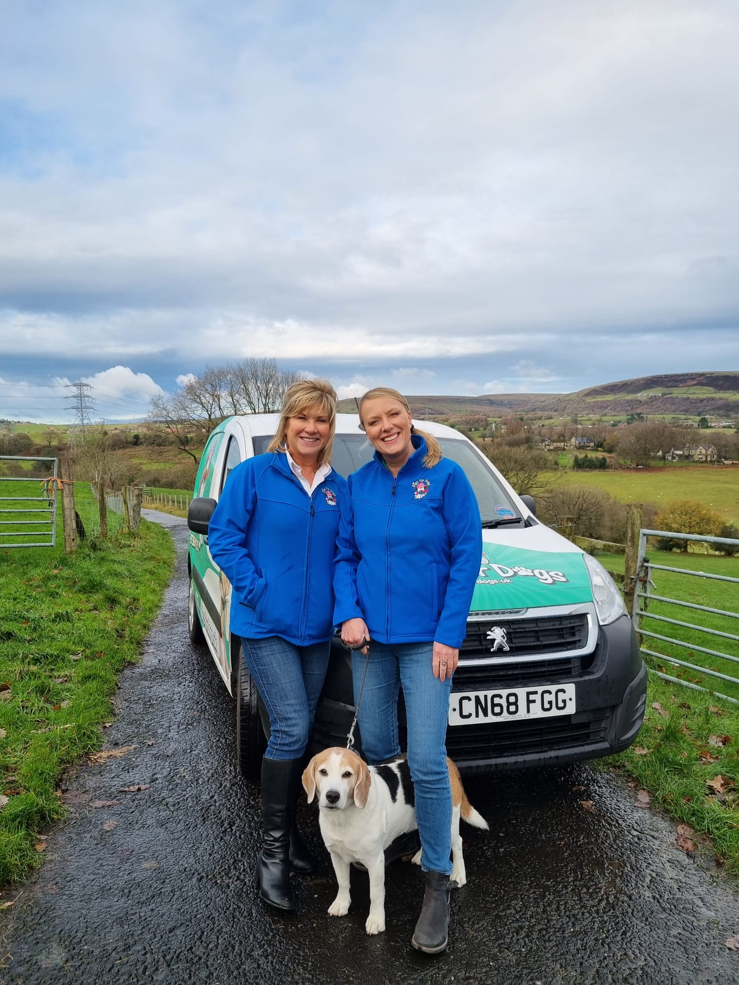 Two Digs for Dogs team members and a beagle beside a branded van