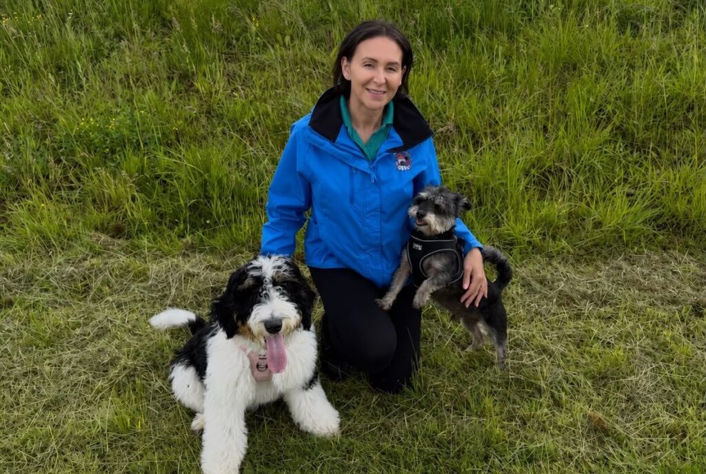 A Digs for Dogs team member kneeling on grass with two dogs